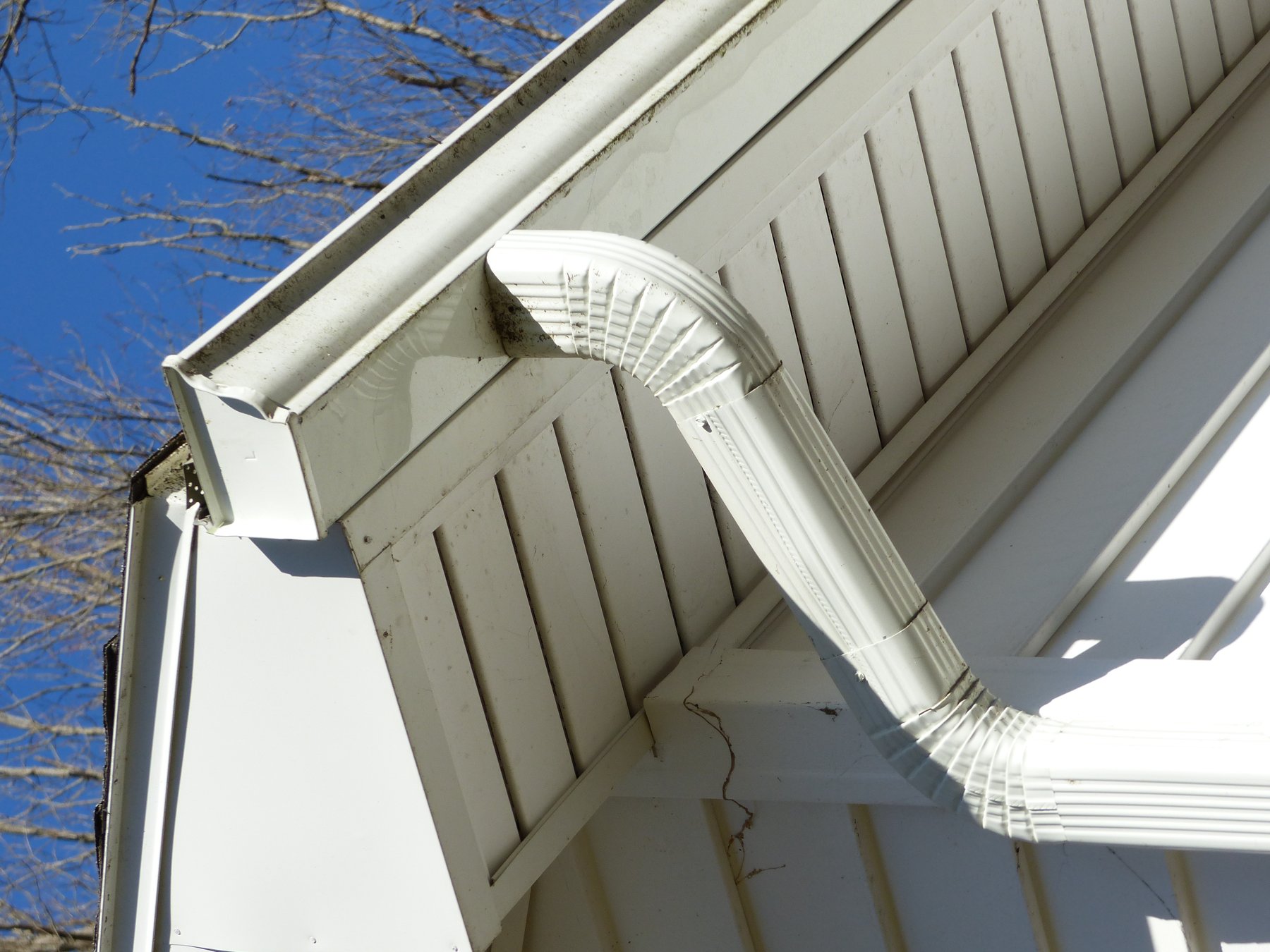Seamless white aluminum gutter and downspout along a steep roof edge